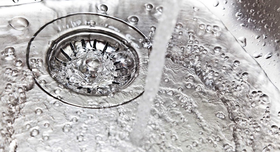Symbolisches Bild mit Spülbecken und fließendem Wasserstrahl.
