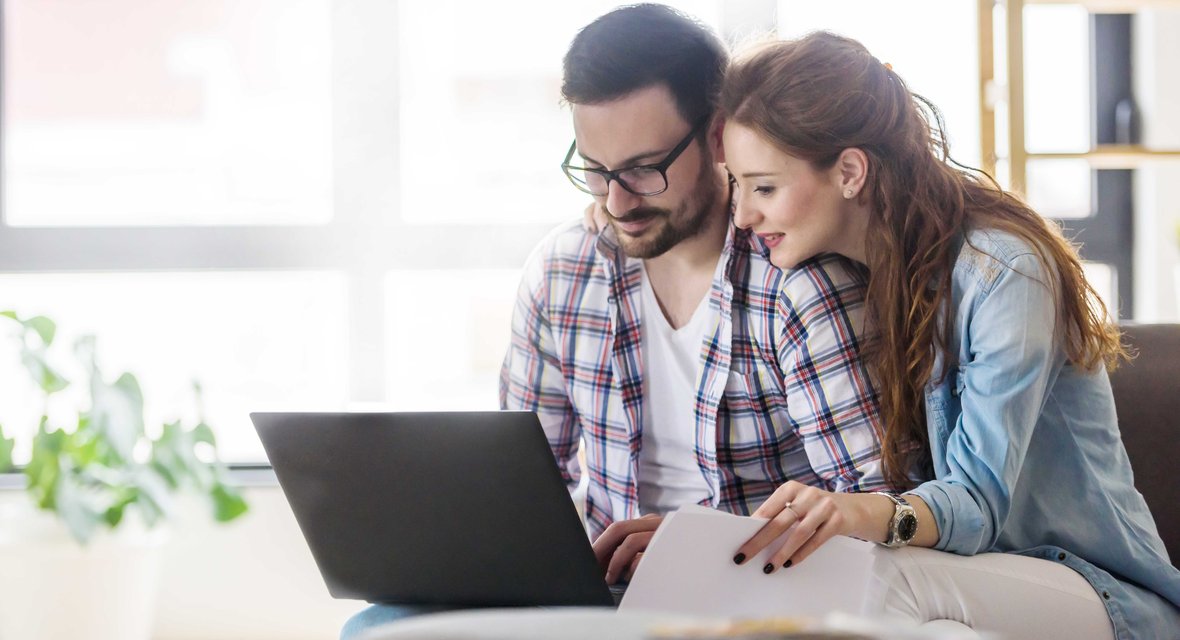 Symbolisches Bild mit zwei Personen vor Laptop sitzend.